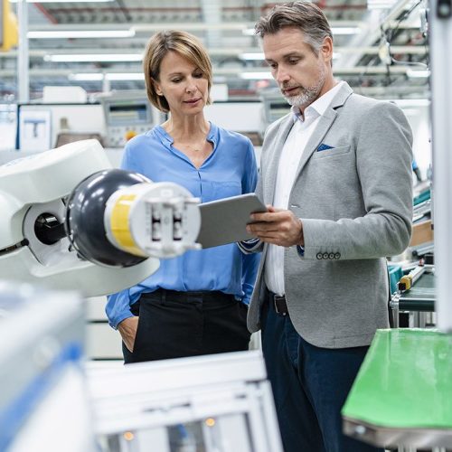 Businessman with tablet and woman talking at assembly robot in a factory Businessman with tablet and woman talking at assembly robot in a factory